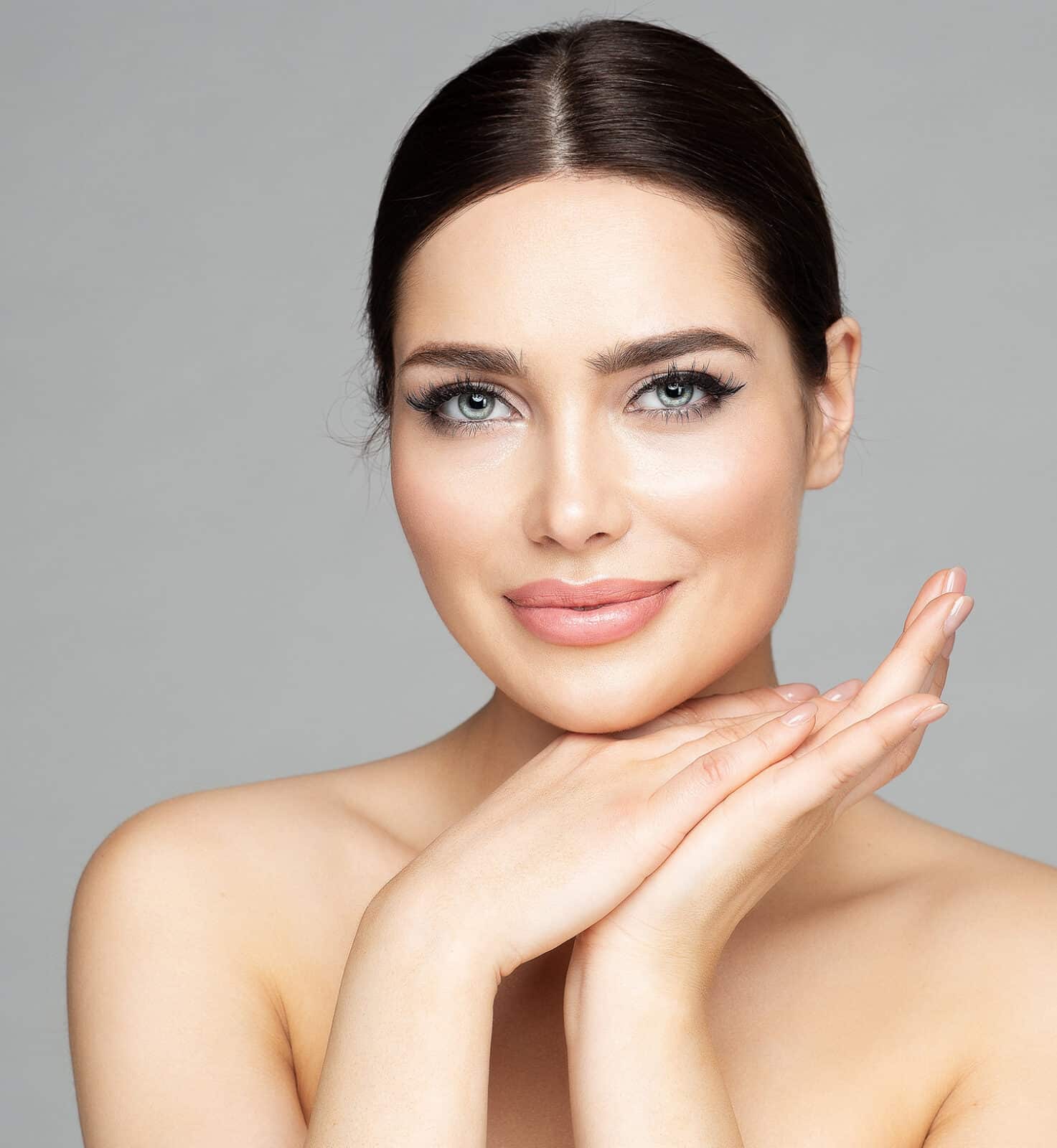 Beauty Woman Face Skin Care. Beautiful Woman Portrait with Full Lips and Long Eyelashes over Gray. Hands Manicure and Facial Treatment Cosmetics. Spa Massage and Face Lift Cosmetology
