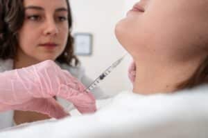 Close-up of a doctor performing a Kybella injection on a young woman’s chin, targeting submental fullness as part of a non-surgical contouring and dermatology treatment.